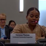 vanessa thomas sits at table with microphone and name card in front of her testifying